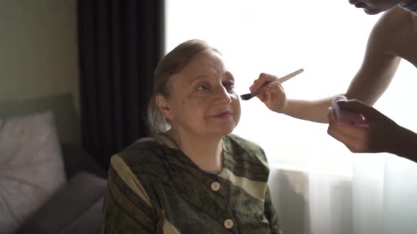 La fille met une poudre sur le visage de sa grand-mère. Jeune femme se maquille sur le visage d'une vieille femme. — Video