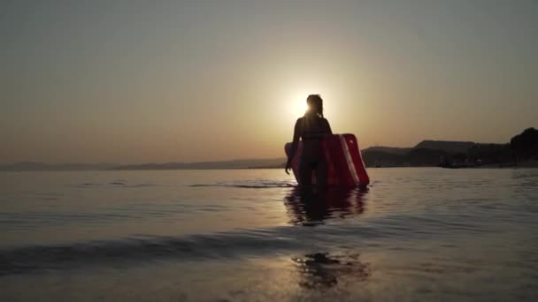 Young girl walks out of the sea with inflatable mattress in her hands and shakes by her hair. Woman walks out of the evening sea with inflatable mattress in her hands and shakes by her hair. — Stock Video