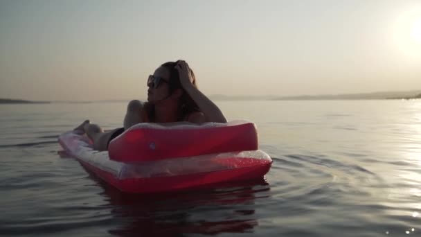 Nahaufnahme eines Mädchens, das auf einer aufblasbaren Matratze im Meer liegt und herumwirbelt. Frau liegt auf aufblasbarer Matratze im Meer und wirbelt darauf herum.. — Stockvideo