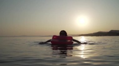 Gece denizinde şişme yatakta yatan ve yüzen bir kızın orta pozu. Denizde şişme yatakta yatan ve yüzen bir kadın..