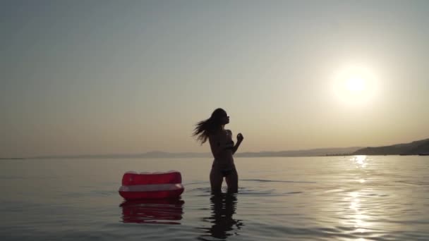 Yong lady shakes her hair while standing into the water with inflated mattress nearby her and then turns around. — Stock Video