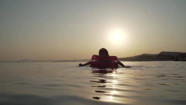 Long shot of girl lying and swimming on the inflatable mattress in the evening sea. Woman lying and swimming on the inflatable mattress in the sea. — Stock Video