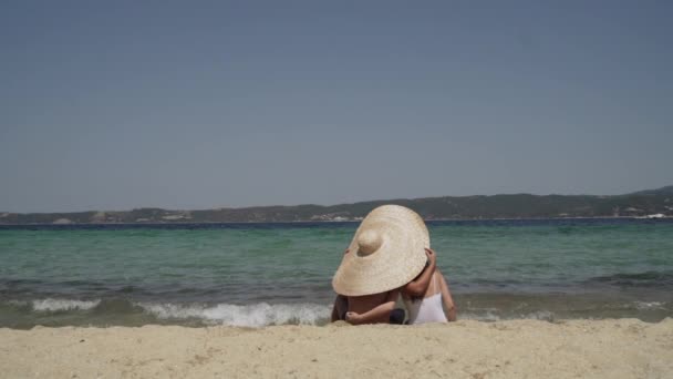 Largo tiro de joven pareja sentada en la arena a la orilla del mar, abrazando y admitiendo la vista. Paisaje marino, romántico. Vacaciones en familia, luna de miel. — Vídeos de Stock