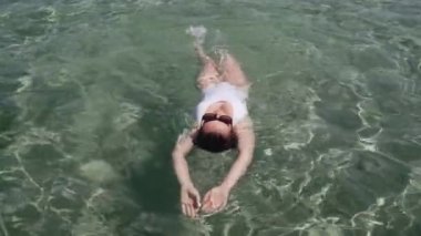 Suda beyaz mayo giymiş bir kadının orta pozu. Genç bayan yüzüyor ve güneşin tadını çıkarıyor. Denizde tatilin tadını çıkaran kadın..