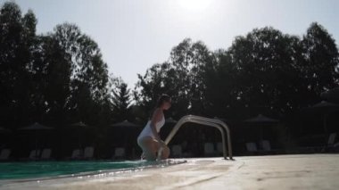 Beyaz mayolu ve güneş gözlüklü genç bayanın yüzme havuzundan çıkarken uzun bir fotoğrafı..