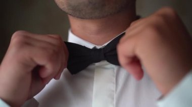 Papyon takan adamı yakından çek. Beyaz gömlekli genç, zarif bir fiyonk giyiyor. Damat düğüne hazırlanıyor..