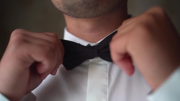 Dichtbij een man die een strikje omdoet. Jonge volwassene in wit shirt met een elegante strik. De bruidegom maakt zich klaar voor de bruiloft. — Stockvideo