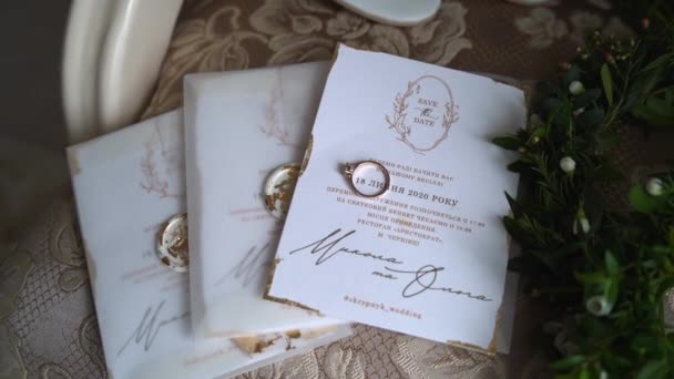 Detailní záběr elegantních svatebních pozvánek. Krásné zlaté prsteny a zeleň. Úžasné detaily a svatební symboly