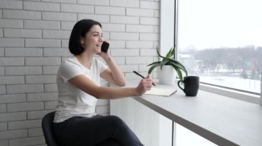 Kısa siyah saçlı genç bayan telefonda konuşuyor. İnternetten sipariş veren yetişkin bir kadın iş adamı gibi görünüyor ve gülümsüyor. Orta resim, online alışveriş, mutlu müşteriler..