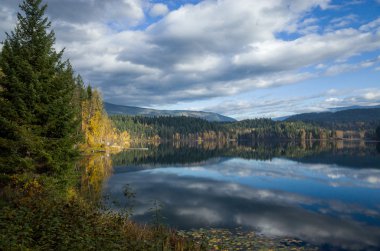 Bulutlu gökyüzü yansıtan sakin dağ gölü