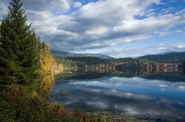 Bulutlu gökyüzü yansıtan sakin dağ gölü