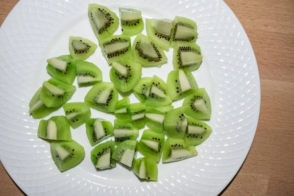 Nahaufnahme von grünen Kiwi-Früchten, in Würfel geschnitten auf einem weißen Teller mit Holzhintergrund — Stockfoto