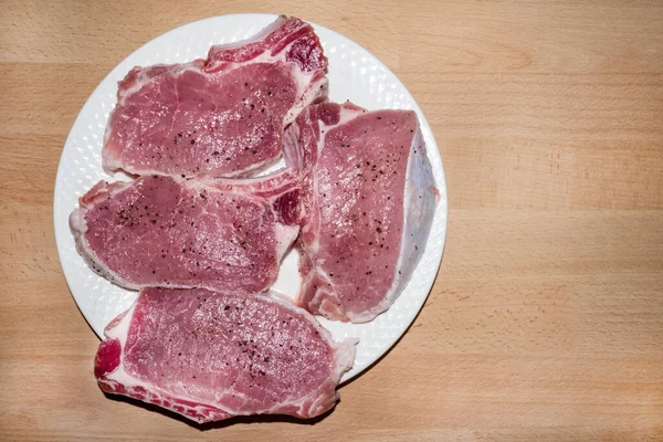 Vier rauwe varkenssteaks met specerijen op wit bord, klaar om te koken — Stockfoto