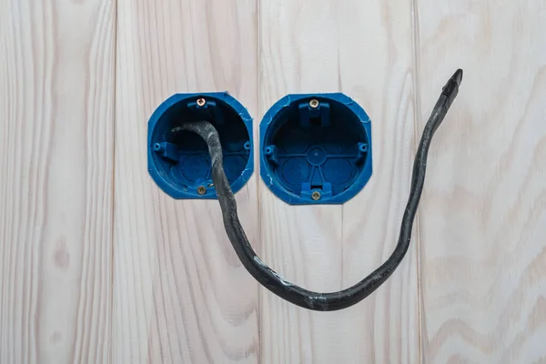 Δύο στρογγυλά μπλε κουτιά τοποθέτησης για τοποθέτηση πρίζες με μαύρο ηλεκτρικό καλώδιο. Σχεδιασμένο για την τοποθέτηση διακοπτών και υποδοχών. Λευκός ξύλινος τοίχος — Φωτογραφία Αρχείου