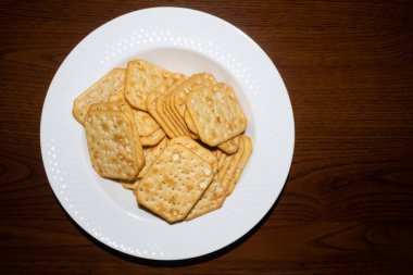 Koyu ahşap masada kuru dereotlu büyük beyaz bir tabak çıtır çıtır kraker.