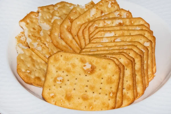 Close up of laid out, squared cheese crackers with spices on white plate — Stock Photo, Image