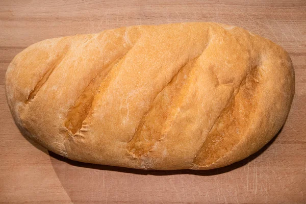 Top view of freshly baked loaf on old scratched wooden cutting board — Stock Photo, Image