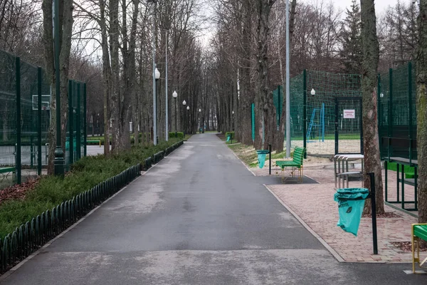 Kharkiv, Ukraine - 17 avril 2021. Allée à Central Park entre terrain de basket et terrain de volley-ball. Bancs et poubelles en bois vert — Photo