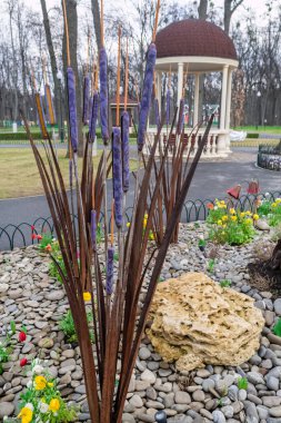 Kharkiv, Ukrayna - 17 Nisan 2021. Çiçek tarlasının ortasına, büyük ve küçük taşlarla çevrili mor ve kahverengi kamışların metal kurulumu. Central Park