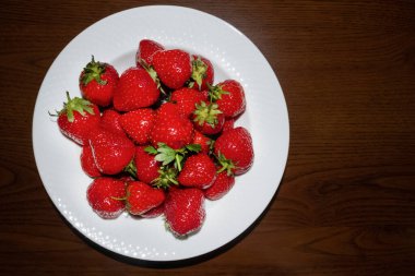 Beyaz tabak, koyu ahşap masada taze kırmızı çilek dolu. Kopyalama alanı