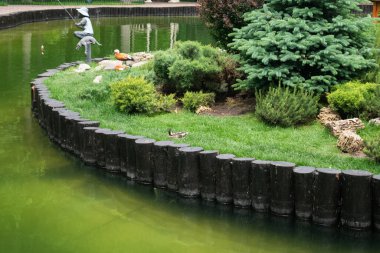 Kharkiv, Ukrayna - 6 Haziran 2021. Ördekler, Central Park 'taki gölde dinleniyorlar. Bir çocuğun metal heykeli, köpekle balık tutuyor.