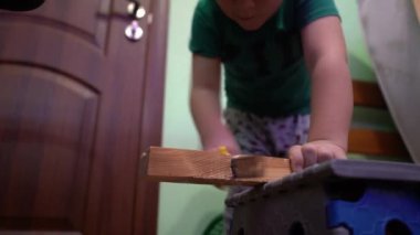 Bir çocuk tahta bir tahtayı demir testeresiyle kesiyor..