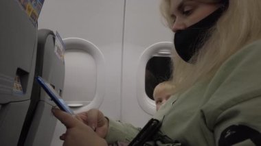 Uçaktaki yolcular uçuş sırasında alet kullanıyorlar. Uçuş sırasında maske takan yolcular ve Covid-19 koronavirüs salgını..