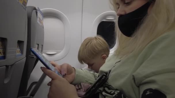 Οι επιβάτες στο αεροπλάνο χρησιμοποιούν συσκευές κατά τη διάρκεια της πτήσης. Επιβάτες με μάσκες κατά τη διάρκεια της πτήσης και η πανδημία του Covid-19 coronavirus. — Αρχείο Βίντεο