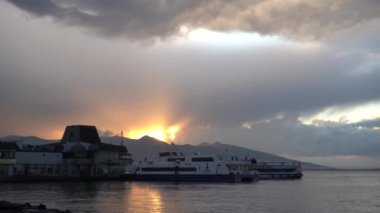 İzmir, Türkiye - Ocak 2021: Konak istasyonundaki motorlu gemilere tepeden bakan güzel gün batımı. Motorlu gemi rıhtımdan ayrılıyor. Gemilerin manzarası ve dağların arkasında güzel bir günbatımı..