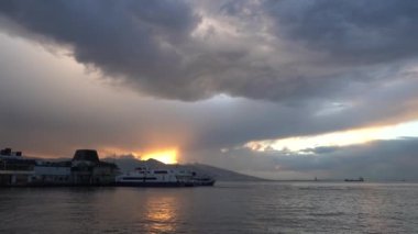 İzmir, Türkiye - Ocak 2021: Konak istasyonundaki motorlu gemilere tepeden bakan güzel gün batımı. Motorlu gemi rıhtımdan ayrılıyor. Gemilerin manzarası ve dağların arkasında güzel bir günbatımı..