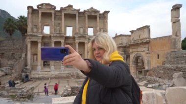 Covid-19 salgını sırasında seyahat etmek. Maskeli bir kadın çekimlerin arka planında selfie çekiyor. Türkiye 'deki antik Yunan kenti Efes' in kalıntıları. Kendi fotoğraflarını çekiyor..