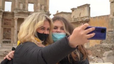 Covid-19 salgını sırasında seyahat etmek. Maskeli bir kadın çekimlerin arka planında selfie çekiyor. Türkiye 'deki antik Yunan kenti Efes' in kalıntıları. Kendi fotoğraflarını çekiyor..