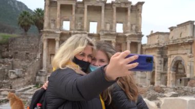 Covid-19 salgını sırasında seyahat etmek. Maskeli bir kadın çekimlerin arka planında selfie çekiyor. Türkiye 'deki antik Yunan kenti Efes' in kalıntıları. Kendi fotoğraflarını çekiyor..