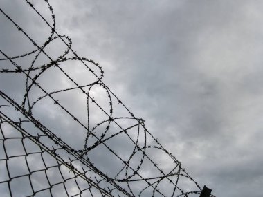 Varşova, Polonya, 1 Haziran 2025: Yasak bir bölgede dramatik bir bulutlu gri gökyüzüne karşı dikenli tellerle çevrili bir tel örgüye yakın çekim