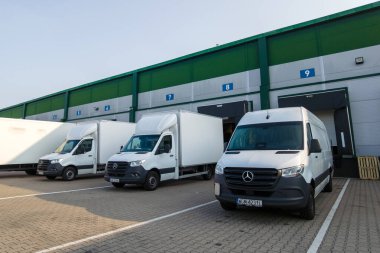 Varşova, Polonya, 1 Haziran 2025: Bir dizi beyaz teslimat minibüsü ve Mercedes-Benz Actros kamyonu açık bir gökyüzü altında lojistik merkezine park edilmiş..