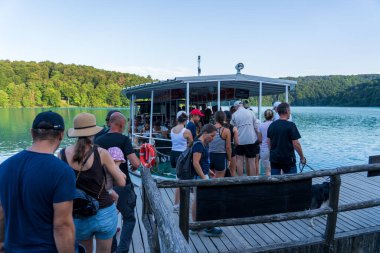 Plitvice Lakes, Hırvatistan - 16 Ağustos 2025: Bir gölün turkuaz sularında seyahat eden yolcularla dolu bir turistik tekne. Arka planda yemyeşil orman olan Ulusal Park manzarası.