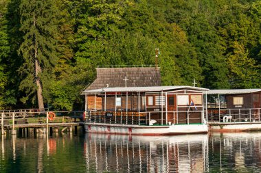 Plitvice Lakes, Hırvatistan - 16 Ağustos 2025: Bir gölün turkuaz sularında seyahat eden yolcularla dolu bir turistik tekne. Arka planda yemyeşil orman olan Ulusal Park manzarası.