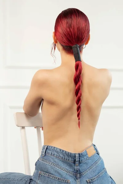 白い部屋のスタジオのポニーテールの赤い髪をした椅子に女の子が腰を下ろして — ストック写真