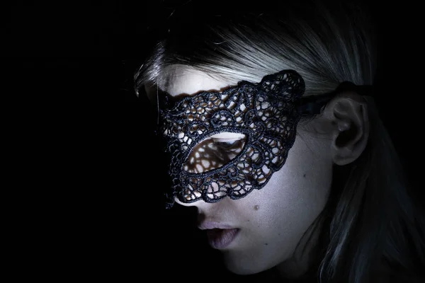 face of a girl in a black lace mask in the dark under low light close up