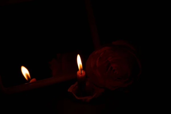 a candle flame and next to one rose in the dark close-up