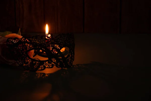 candle flame and next to one rose and lace face mask for carnival in the dark close-up