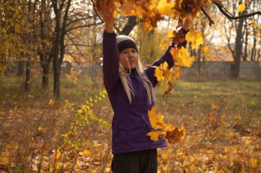 Sonbahar parkında sarı yapraklar içinde gün boyunca Ukrayna 'da düşen bir kız.