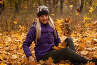 Sonbahar parkında sarı yapraklar içinde gün boyunca Ukrayna 'da düşen bir kız.