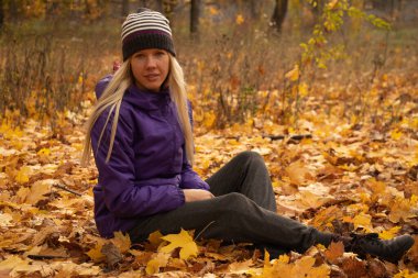 Sonbahar parkında sarı yapraklar içinde gün boyunca Ukrayna 'da düşen bir kız.