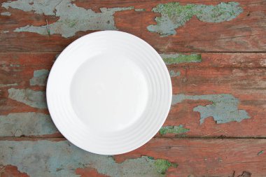 Beyaz cam boş tabak, dışarıdaki eski boyanmış ahşap tahta üzerinde duruyor.