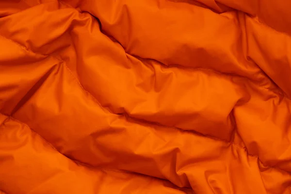 orange fabric of a warm puffed jacket as a background close up