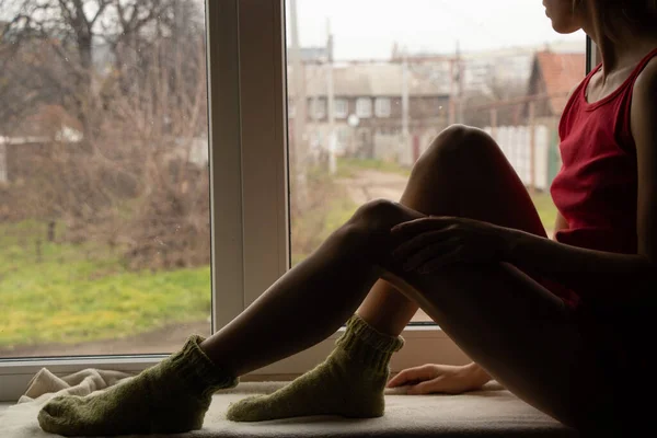 young girl sits in the winter on the window alone on vacation, home self-isolation