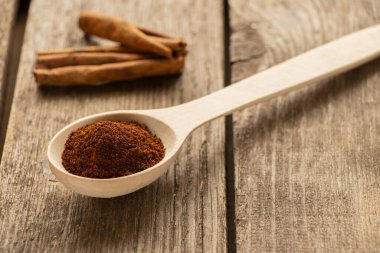 Tahta kaşık, öğütülmüş kahve ve tarçınlı çubuklar güneş ışığında ahşap masada.