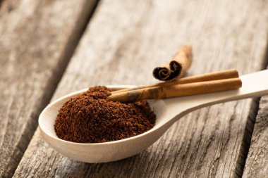 Tahta kaşık, öğütülmüş kahve ve tarçınlı çubuklar güneş ışığında ahşap masada.