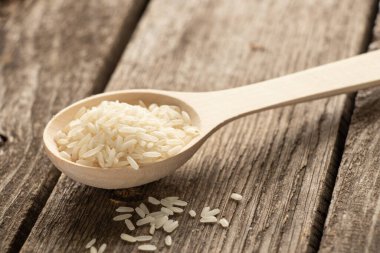 Tahta bir kaşık ve çiğ beyaz pirinç, gün ışığında ahşap bir masada.